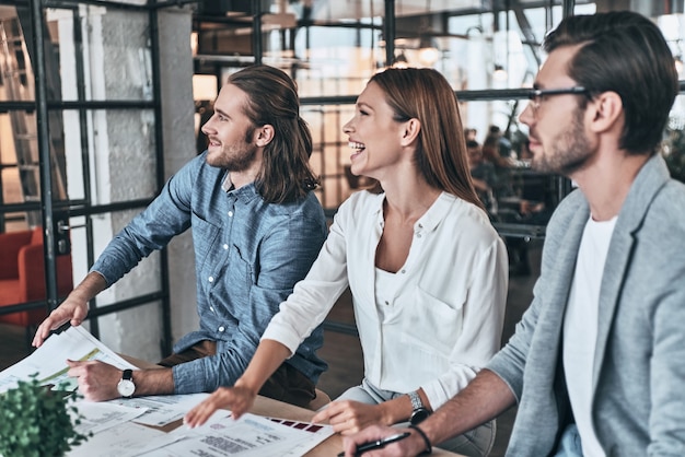 Leidenschaftlich für ihr Projekt. Gruppe junger Geschäftsleute, die etwas diskutieren und lächeln, während sie im Büro sitzen sitting