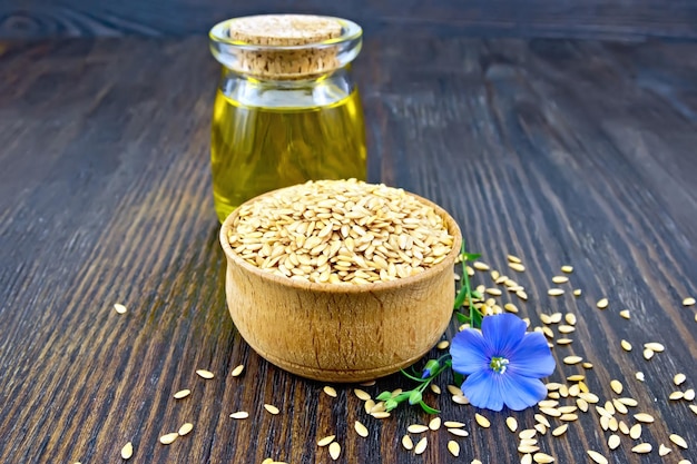 Leinensamen sind weiß in einer Schüssel Leinöl in einem Glasgefäß und blaue Flachsblume auf einem Holzbretthintergrund