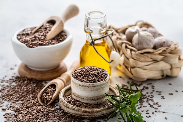 Leinsamenöl in einer Flasche und Keramikschale mit braunen Leinsamen und Holzlöffel auf einem weißen