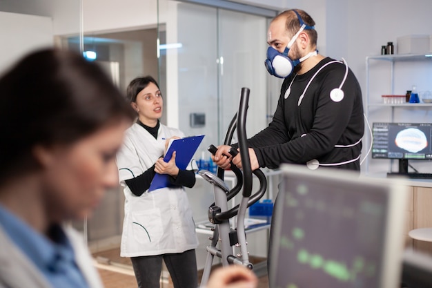 Leistungssportler, der in Laborwissenschaften läuft, testet die Ausdauer mit Maske und Elektroden, Biomechanik-Sensoren. Cardio-Untersuchung. Trainingssensoren zur Fitnessmessung.