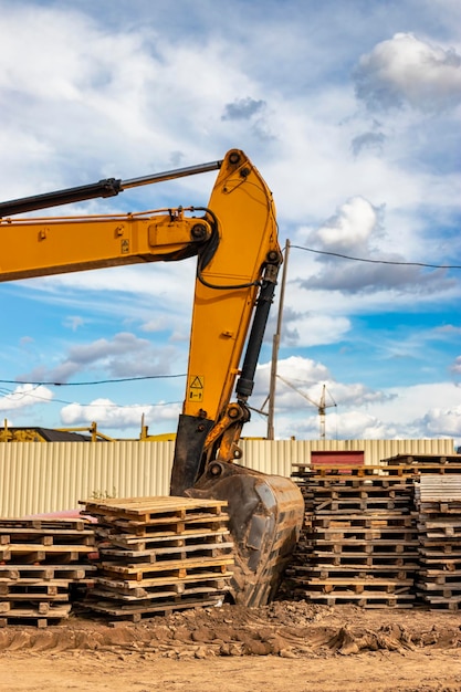 Leistungsstarke Bagger auf einer Baustelle gegen einen blauen bewölkten Himmel Erdbewegungsmaschinen für den Bau Bagger unter Holzpaletten