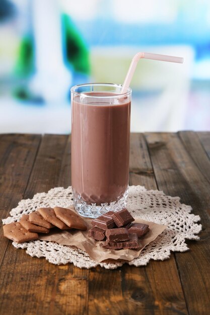 Foto leite com chocolate em vidro na mesa de madeira no fundo brilhante