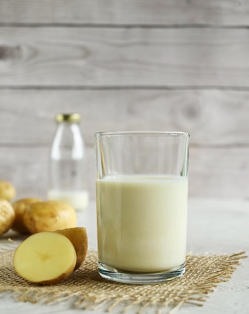 Leite de batata vegano em um copo de serapilheira e batatas no fundo de uma mesa de madeira não lácteas espaço de cópia de leite alternativo