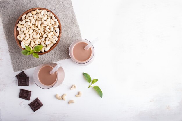 Leite de chocolate não orgânico do caju da leiteria na placa de vidro e de madeira com porcas de caju em um concreto cinzento.