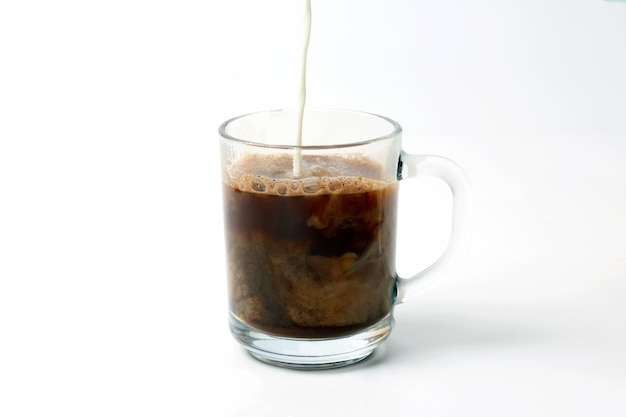 Leite derramado em uma xícara transparente de café preto