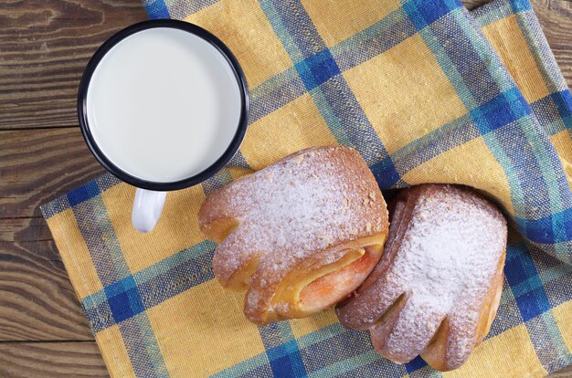 Leite em uma caneca esmaltada com pãezinhos doces na mesa