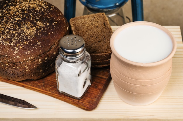 Leite em uma panela de barro, pão, sal em uma tábua de cortar. Natureza morta em estilo rústico