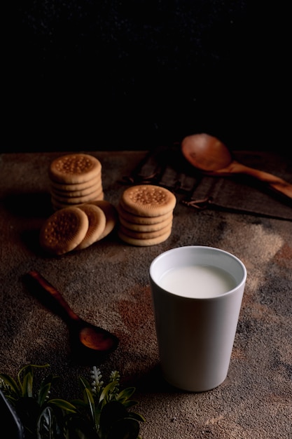 Leite fresco com biscoitos caseiros em uma mesa de madeira, fundo escuro.