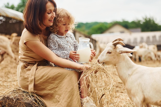 Leite natural fresco Jovem mãe com sua filha está na fazenda no verão com cabras