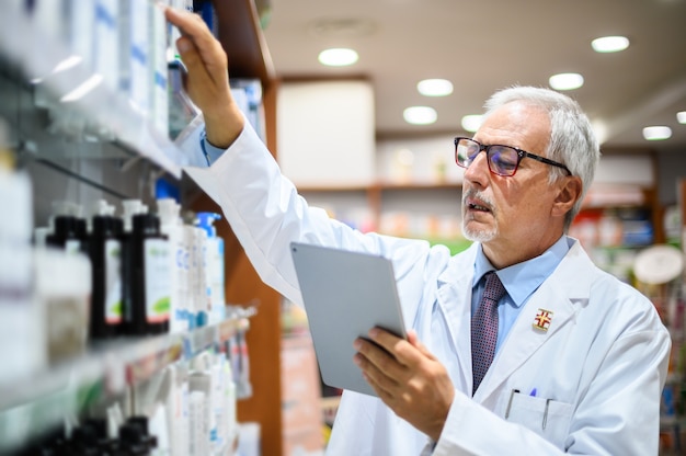 Leitender Apotheker, der in einem Regal in seinem Geschäft nach einem Produkt sucht und ein Tablet verwendet