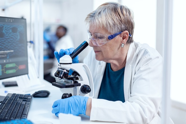 Leitender Chemiker, der genetische Untersuchungen mit dem Mikroskop durchführt. Älterer Forscher, der wissenschaftliche Forschung in einem sterilen Labor mit moderner Technologie durchführt.