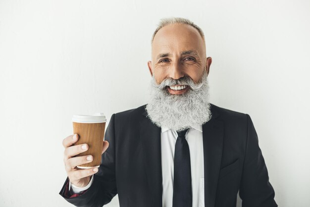 Leitender Geschäftsmann mit Pappbecher Kaffee auf hellem Hintergrund