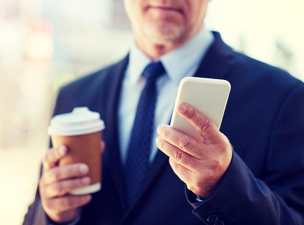 leitender Geschäftsmann mit Smartphone und Kaffee