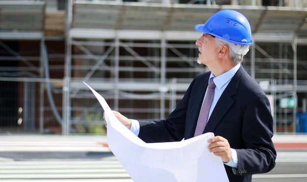 Leitender Ingenieur, der eine Lichtpause I vor einer Baustelle liest