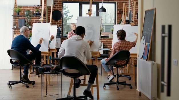 Leitender Lehrer, der die Schüler beaufsichtigt, im Kunstunterricht Vasenmodelle auf Leinwand zu zeichnen. Ältere Frau, die Menschen beim Zeichnen von Meisterwerkskizzen mit Bleistift für Bildungswachstum im Workshop betrachtet.