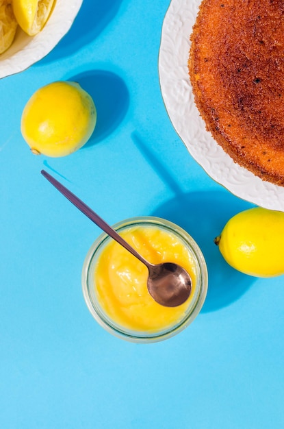 Lemon Kurd casero en un frasco de vidrio con cuchara sobre fondo azul con limones frescos enteros y en rodajas