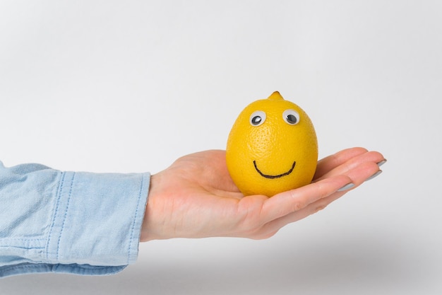 Lemonsmiley engraçado com olhos arregalados, deitado na palma da mão no fundo branco