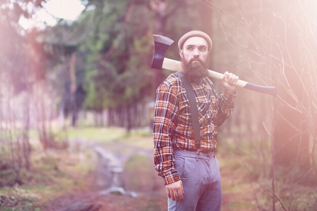 Un leñador barbudo con un hacha grande examina el árbol antes de talarlo.