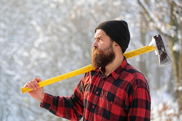 Leñador en el bosque con un hacha Hombre barbudo con sombrero con un hacha Hombre guapo hipster Leñador brutal hombre barbudo con barba y bigote en el día de invierno bosque nevado