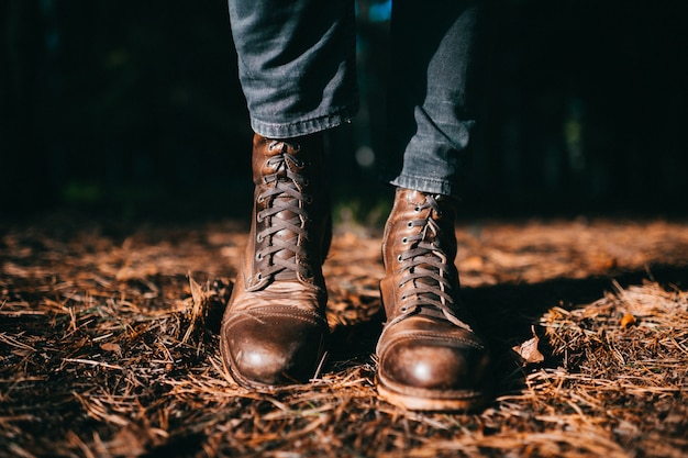 Foto leñador extraño en botas de madera de cuero áspero masculino hipster vintage de pie en el bosque de otoño en el suelo con agujas de abeto naranja seco.