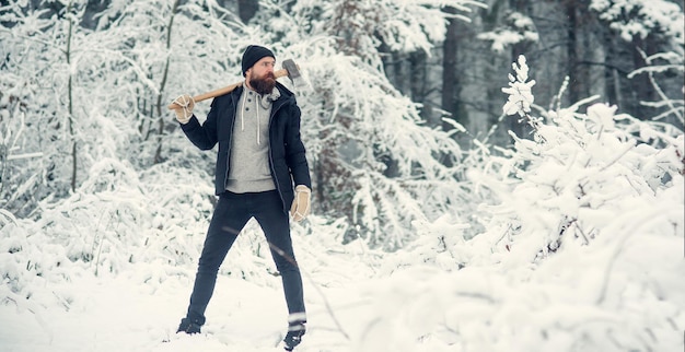 Leñador sostiene hacha hipster con barba en cara seria con hacha brutal leñador en invierno al aire libre