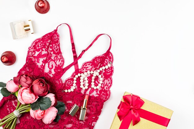 Lencería de encaje rojo de mujer con caja de regalo, flores, maquillaje artículos sobre fondo blanco. Postal para el día de la mujer.