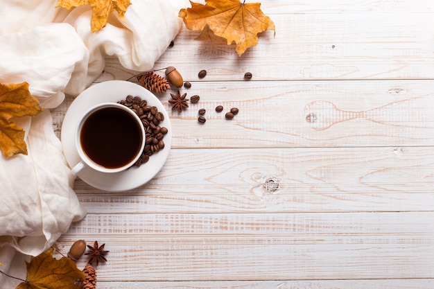 Lenço branco, uma xícara de café com grãos de café espalhados, folhas amarelas secas em uma mesa de madeira. Humor de outono, copyspace.