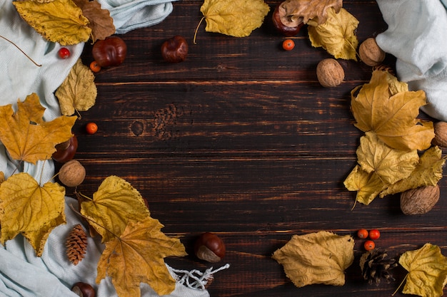 Foto lenço, castanhas, nozes e folhas secas em uma mesa de madeira. fundo de outono, copyspace.