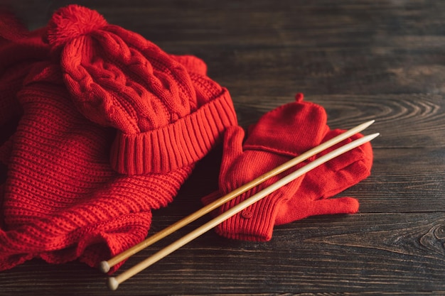 Lenço de chapéu vermelho de malha luvas de malha e agulhas de tricô de madeira em fundo de madeira Artesanato de hobby Conceito de bordado de tricô
