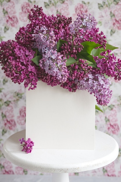 Lençol branco em flores lilás violetas roxas desabrochando em um suporte branco sobre um fundo floral. Cartão de felicitações, lugar para texto, simulação