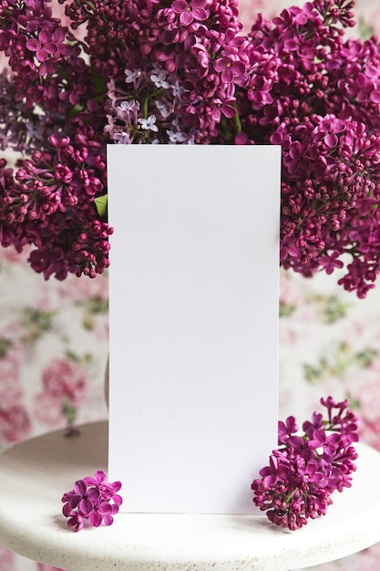 Lençol branco em flores lilás violetas roxas desabrochando em um suporte branco sobre um fundo floral. Cartão de felicitações, lugar para texto, simulação