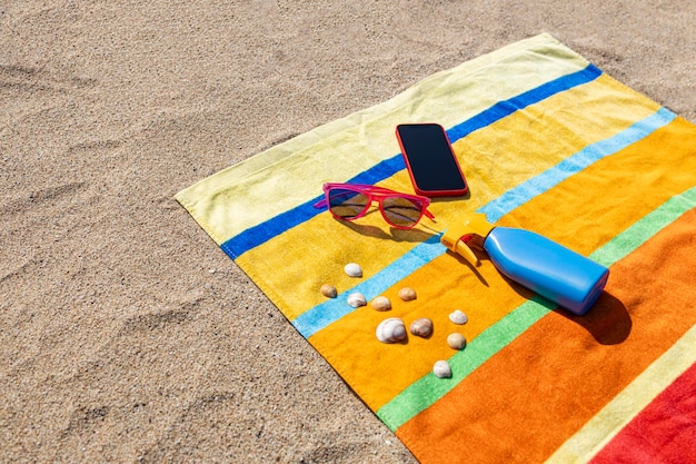 Foto lençol, óculos de sol e telefone inteligente na praia, conceito de verão.