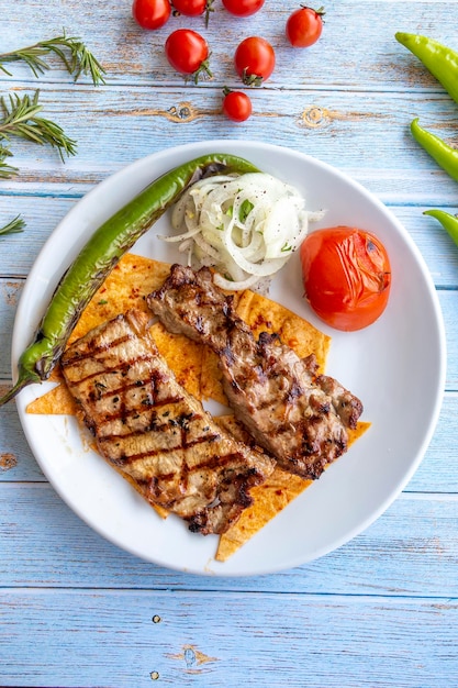 Lendensteak auf blauem Holzhintergrund mit gerösteten Tomaten, Zwiebeln und Paprika