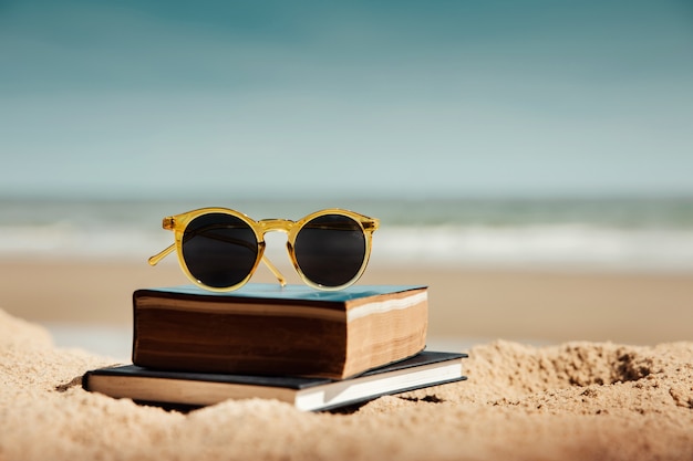 lendo o livro ao ar livre no conceito de verão. livro e óculos de sol na areia da praia em dia ensolarado