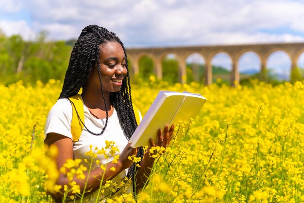 Lendo um livro na natureza uma garota de etnia negra com tranças um viajante em um campo de flores amarelas