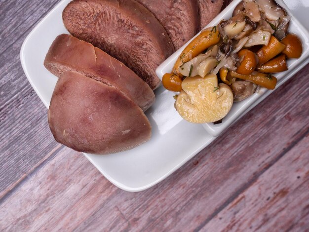 Lengua de cerdo de ternera hervida con champiñones tiro de estudio aislado sobre fondo de madera