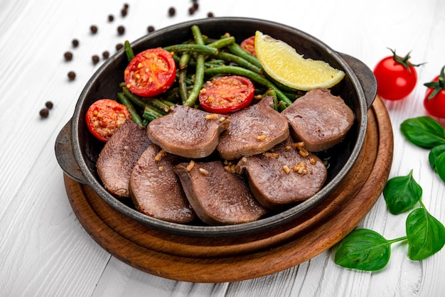 Lengua de ternera frita con judías verdes y tomates en una sartén