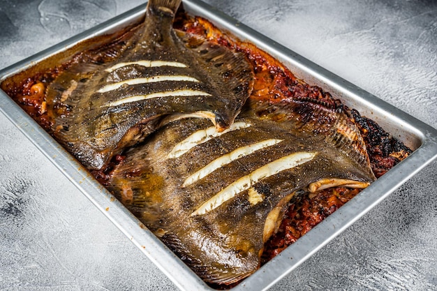 Lenguado plano de pescado asado en salsa de tomate en bandeja de horno. Fondo blanco. Vista superior.