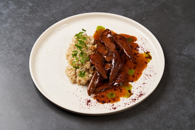 Lenguas de cordero al horno con gachas de bulgur picante en un plato blanco