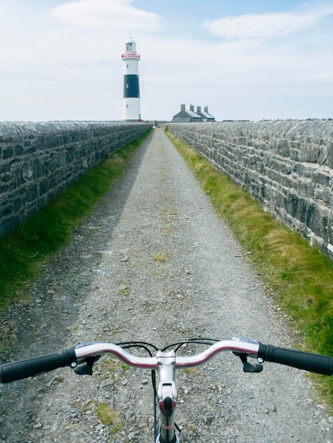 Lenker eines Fahrrads auf einer Straße, die zu einem Leuchtturm auf einer irischen Insel führt