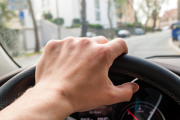 Lenkrad mit Fahrerhand darauf im modernen Autoinnenraum mit Blick auf die Straße