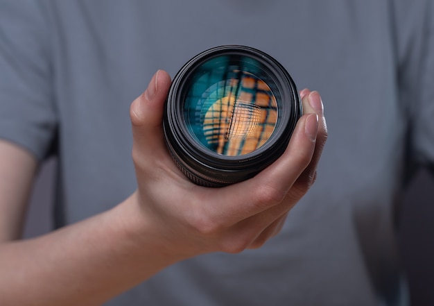 Lente de câmera digital moderna com belo reflexo de estúdio nas mãos da mulher, close-up.