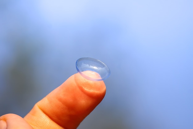 Lente de contato transparente na ponta do dedo em fundo de natureza turva de verão verde.