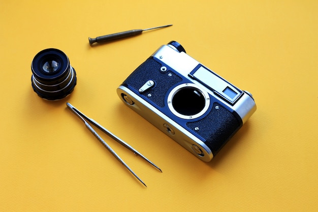 Lente y herramientas vintage, pinzas y un destornillador con papel amarillo, reparación de la cámara