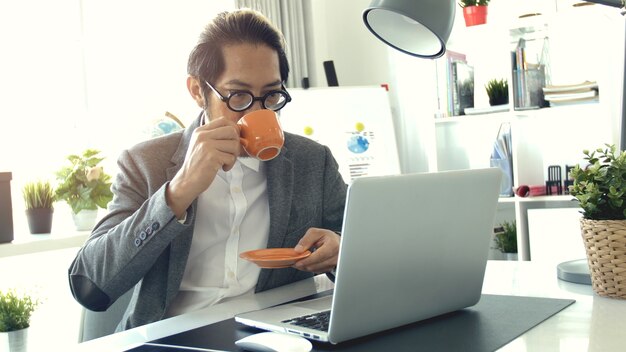 Lente que lleva asiática del hombre de negocios en oficina.