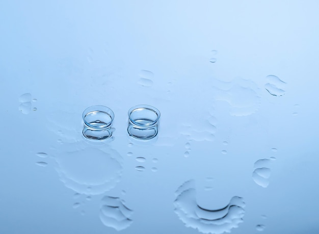 Lentes de contato para os olhos no vidro entre as gotas de água em equipamento óptico azul