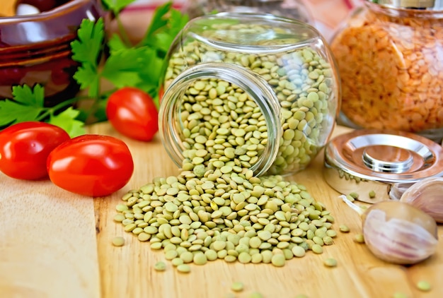 Lentilhas verdes em frasco de vidro, salsa, alho, tomate, panela de barro, guardanapo no fundo de tábuas de madeira