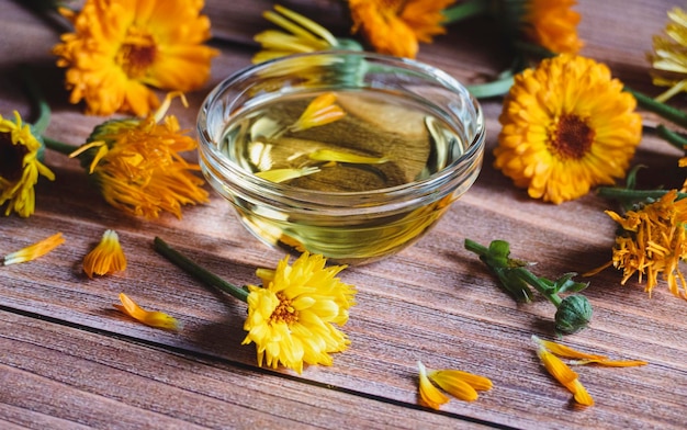 Óleo cosmético Calendula officinalis flores secas e frescas de calêndula na mesa de madeira