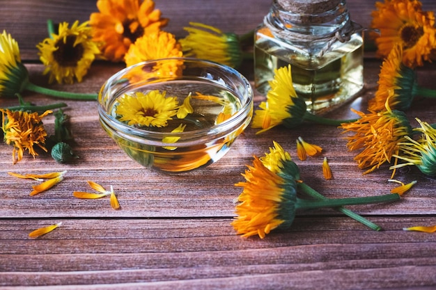 Óleo cosmético Calendula officinalis flores secas e frescas de calêndula na mesa de madeira