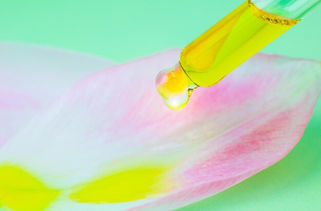 Óleo cosmético com uma pipeta em um fundo verde Feche a gota líquida pingando na pétala de uma flor de tulipa rosa Medicina de beleza e conceito de saúde Foto macro Cosméticos ecológicos naturais